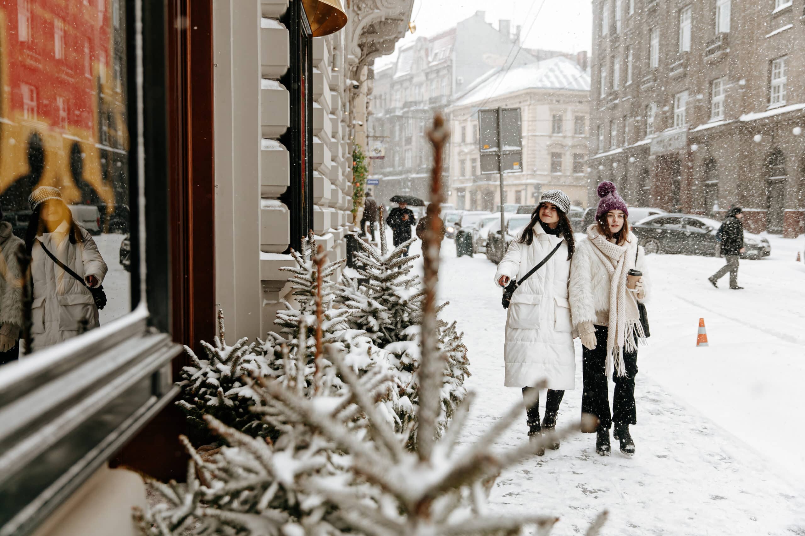women dressed in white jacket, warm hats and scarf walking on street during snowfall